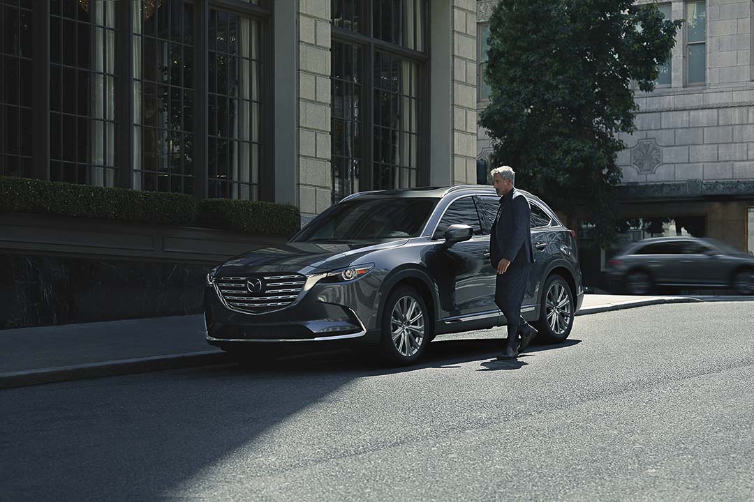 Homme au point de monter à bord du Mazda CX-9 2021.5 stationné au bord d'un trottoir en ville