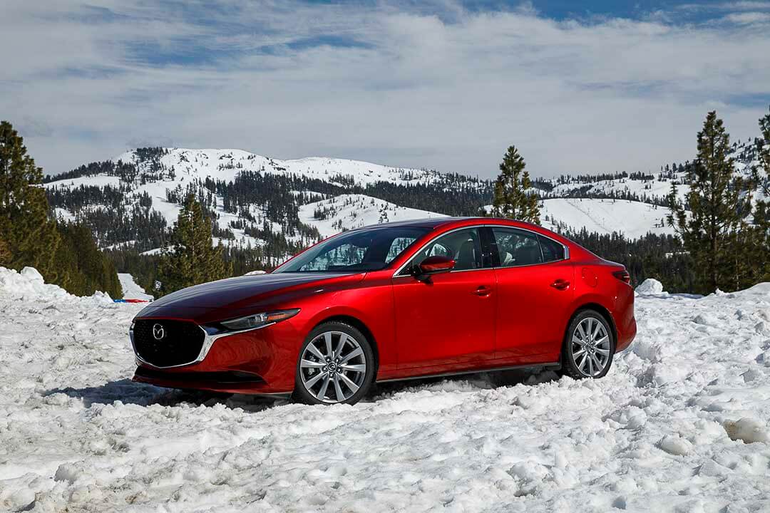 Vue latérale 3/4 avant d'un Mazda3 2021 rouge garé dans une montagne enneigée