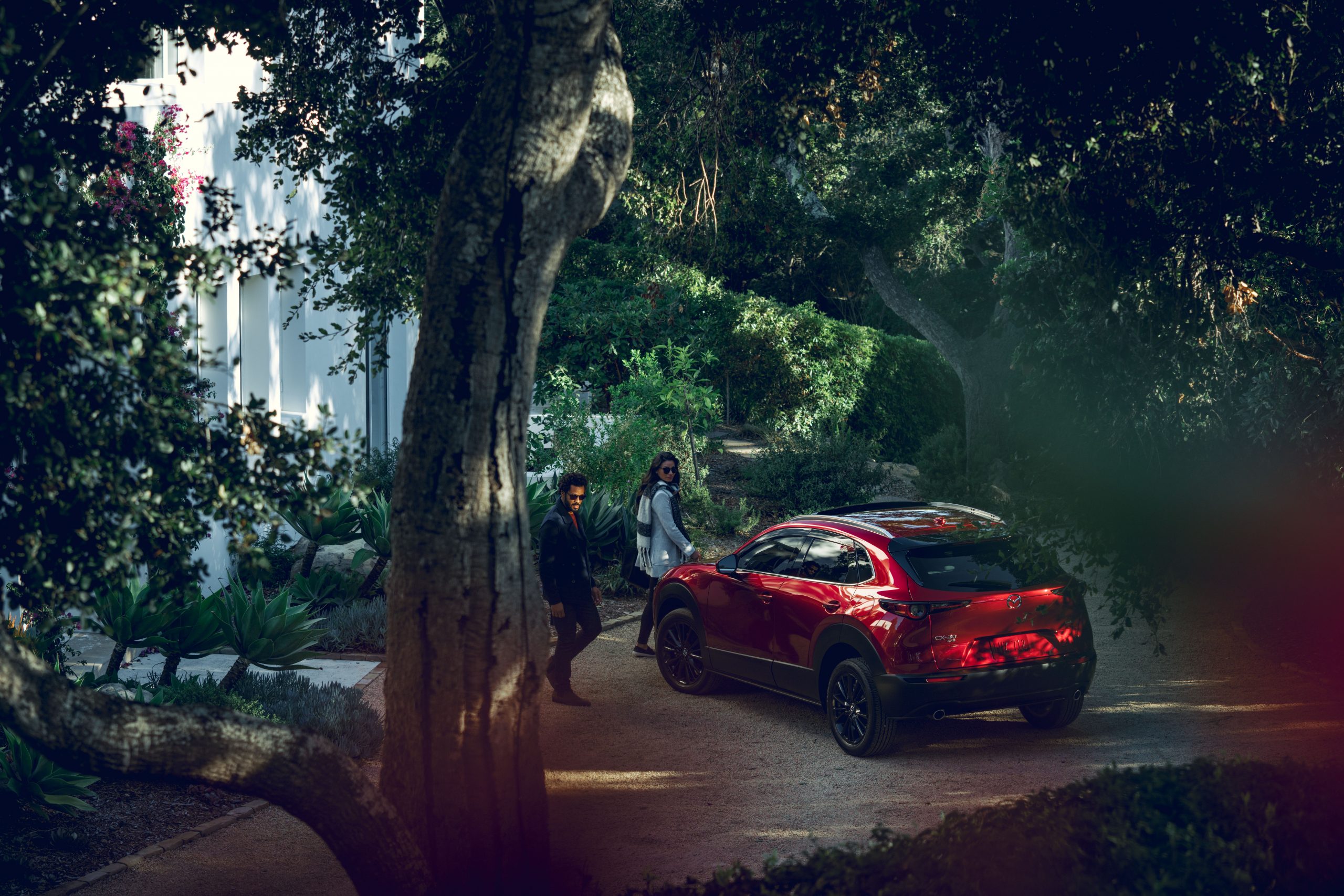 un couple à côté du Mazda CX-30 2020 entre leur maison et une forêt